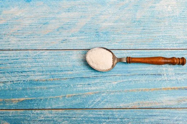 Cuchara con sal sobre un fondo de madera azul . — Foto de Stock