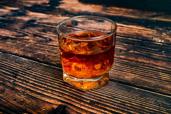 Alkohol egy üveg serlegben fából készült háttérrel, konyak, whisky, brandy jéggel. — Stock Fotó