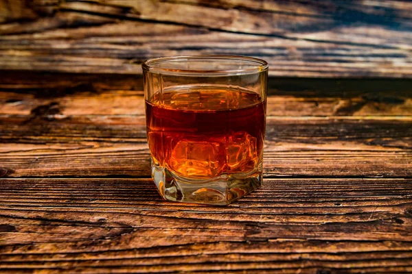 Álcool em uma taça de vidro em um fundo de madeira, conhaque, uísque, conhaque com gelo . — Fotografia de Stock