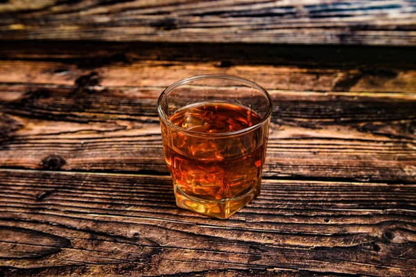 Alcool dans un gobelet en verre sur fond bois, cognac, whisky, brandy avec glace . — Photo