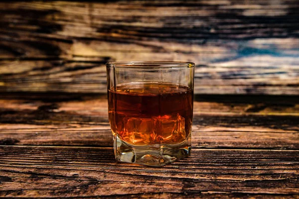 Alkohol w szklanym kielichu na drewnianym tle, koniak, whisky, brandy z lodem. — Zdjęcie stockowe