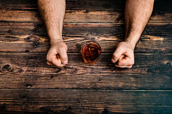 Um homem aperta os punhos, impedindo-se de beber álcool numa mesa de madeira. O conceito de alcoolismo e dependência de álcool . — Fotografia de Stock