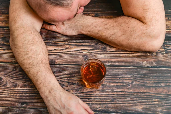 П'яна людина зі склянкою алкоголю лежить на дерев'яному столі. Поняття алкоголізму та алкогольної залежності . — стокове фото