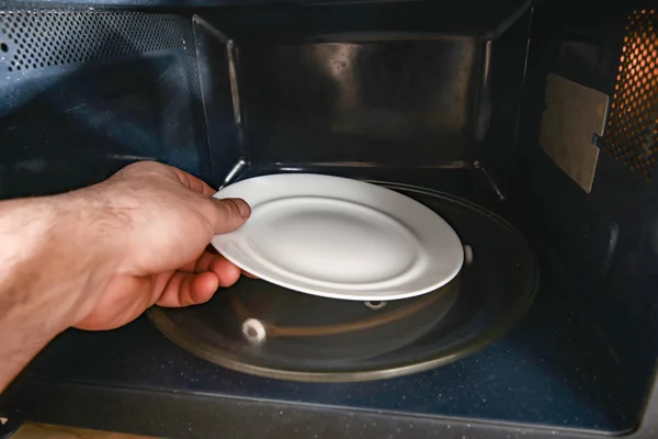 A man puts an empty white plate in the microwave. — Stock Photo, Image