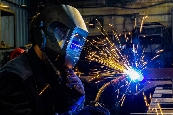 Een arbeider in de lasindustrie met een beschermend masker maakt metaal met een lasmachine. — Stockfoto