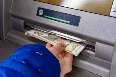 A woman at an ATM withdraws cash hryvnias in Ukraine, 100 and 500 hryvnia notes.