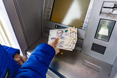 A woman at an ATM withdraws cash hryvnias in Ukraine, 100 and 500 hryvnia notes.