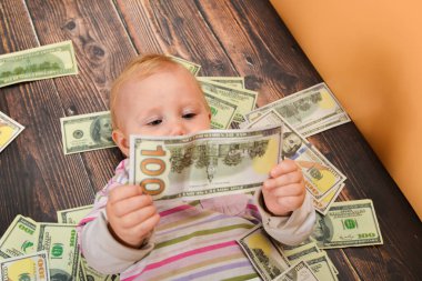 A small child examines a hundred-dollar crumpled bill, lying on the money. The concept of wealth and financial independence.