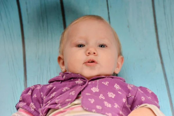 Little girl lies on a blue wooden background and looks at the camera. — Stockfoto