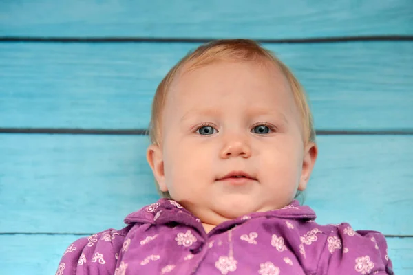 Little girl lies on a blue wooden background and looks at the camera. — Stock Photo, Image