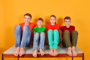 Four children squatting barefoot, a bright colorful juicy photo of teenagers sitting in colored clothes.