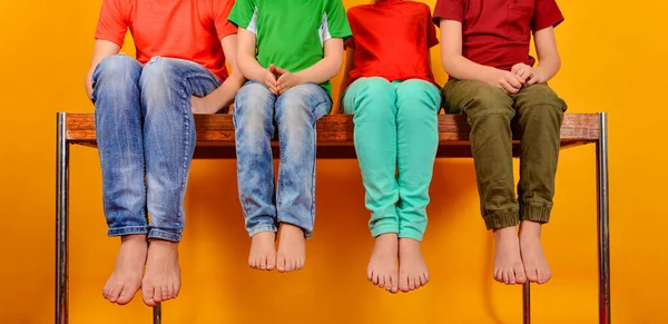 Les enfants en vêtements lumineux et colorés sont assis pieds nus avec leurs jambes suspendues au fond . — Photo