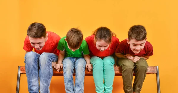 Jongens en een meisje zitten samen en kijken onder hun voeten. — Stockfoto