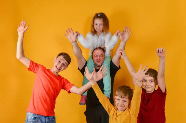 Otec a čtyři radostné děti zvedli ruce, dcera seděla mému otci na ramenou. Vtipné a zábavné krásné děti v barevných šatech. — Stock fotografie