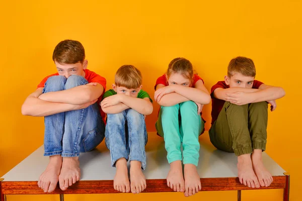 Barefoot children sit with their legs crossed and hugging their knees. Four children bowed their heads and peek out from behind their knees. — Stockfoto