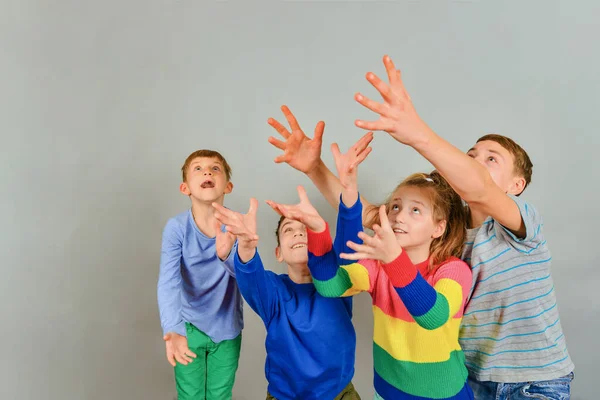 Emotional children pull their hands up in the hope of catching something, four children in colored clothes. Place for advertising and text. — 스톡 사진