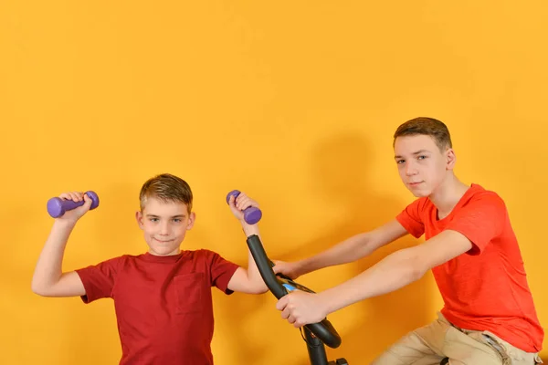 Deux frères sportifs font des exercices cardio, un garçon est bizarre avec des haltères, l'autre est assis sur un vélo stationnaire . — Photo