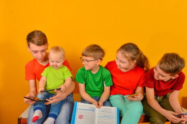 Küçük bir çocuk akıllı telefonuyla oturuyor, diğer çocuklar ona bakıyor..