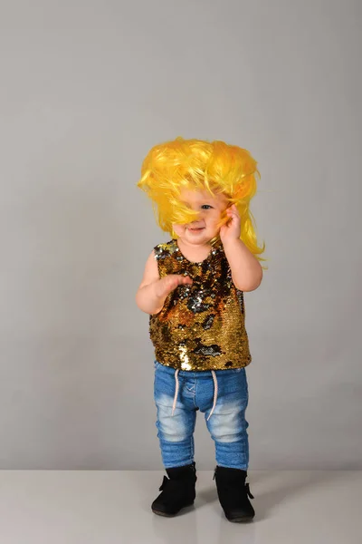 Roczna dziewczynka w żółtej peruce. Małe dziecko w dżinsach i cekinach pozuje w agencji modelek. — Zdjęcie stockowe