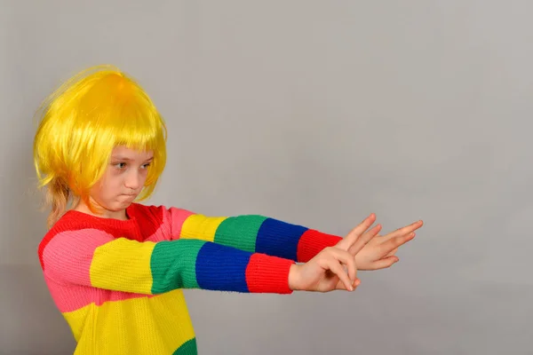 Ein Mädchen mit gelber Perücke zeigt auf einen Platz für ein Werbeprodukt, ein helles Kind auf grauem Hintergrund. — Stockfoto