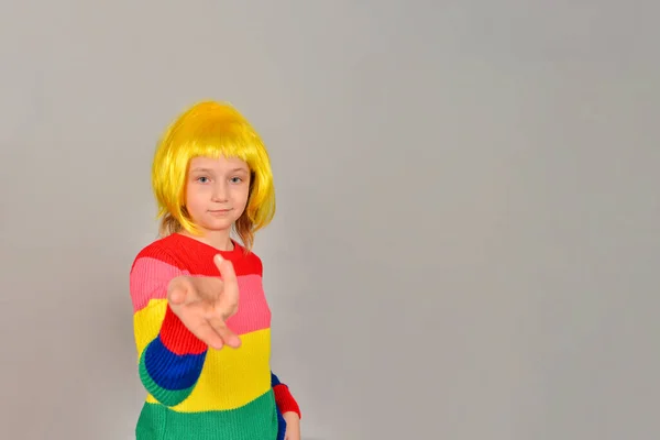 A girl in a yellow wig points to a place for an advertising product, a bright colored child on a gray background. — Stock Photo, Image