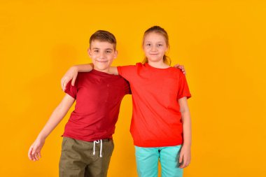 Kırmızı tişörtlü bir çocuk sarı arka planda sarılıp duruyor. Neşeli çocuklar, kardeşlerim.