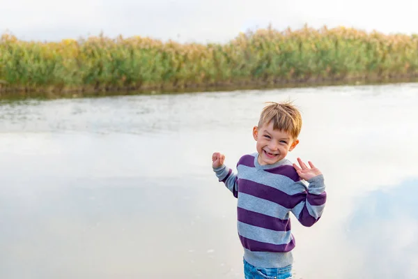 A joyful and positive child stands on the bank of the river and — Stockfoto