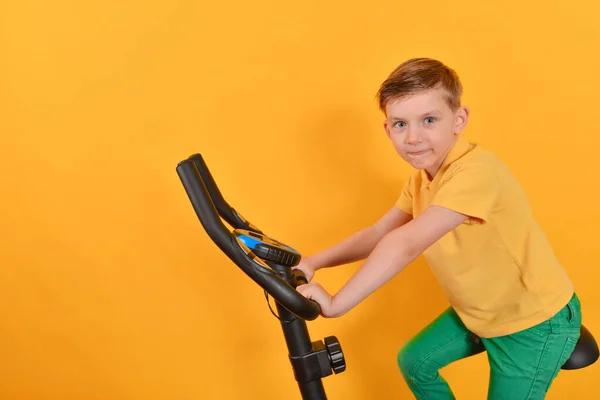 A criança entra para esportes em uma bicicleta estacionária, aptidão para crianças . — Fotografia de Stock