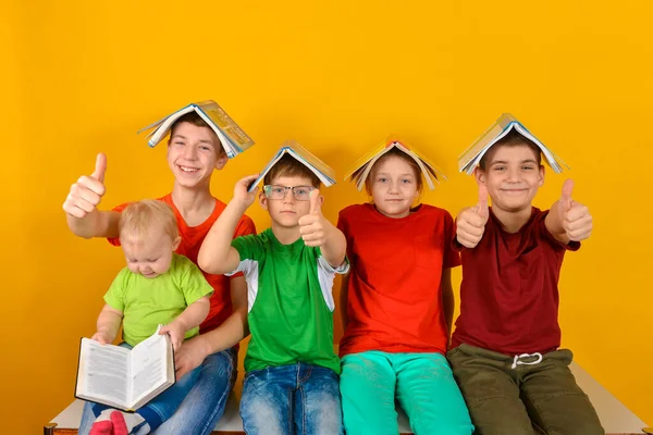 Dzieci siedzą z książką na głowach i trzymają kciuk w górze. Koncepcja wychowania rodzinnego w domu i chęć uczenia się wiedzy. — Zdjęcie stockowe