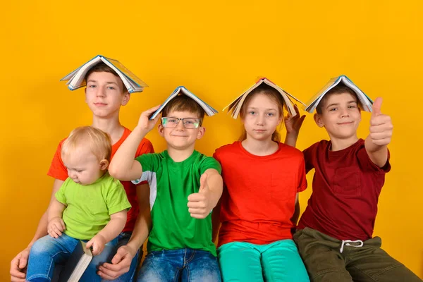 Barn sitter med en bok på huvudet och håller tummen upp. Begreppet familjepedagogik i hemmet och viljan att lära sig mer. — Stockfoto