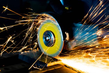 The worker cuts the part with an angle grinder, the abrasive wheel produces sparks when cutting clipart