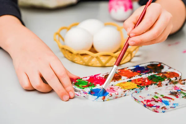 Children paint eggs for Easter, paints draw patterns on a white egg.