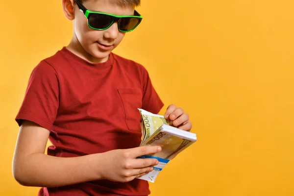 サングラスの男の子は バンドル内の紙幣 黄色の背景に通貨を持つ魅力的でスタイリッシュな子供を考えています — ストック写真