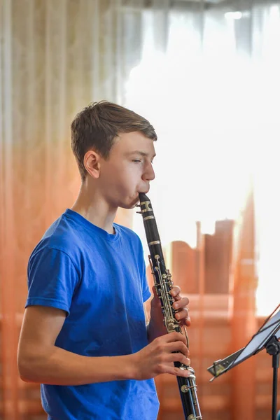 The guy plays the clarinet, looks at the music and plays music in a music school.