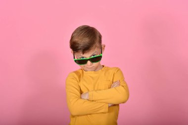 Kameraya poz veren göz kamaştırıcı ve şık bir çocuk. Güneş gözlüklü, sarı elbiseli, pembe arka planda bir model..