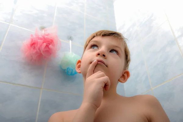 The child in the shower room thinks what kind of washcloth he should choose and what he will do now.