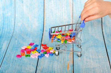 Adamın elinde çok renkli harflerle bir tramvay var. Mavi ahşap arka planda alfabe olan bir tüketici sepeti.