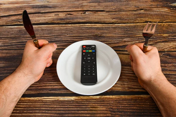 The remote control from the TV lies on a plate, information from the TV instead of food, the concept of brainwashing by the media.