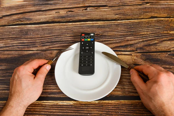 The remote control from the TV lies on a plate, information from the TV instead of food, the concept of brainwashing by the media.