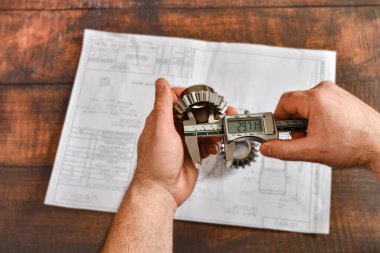 Çalışan bir mühendis, elektronik vernier kalibreli bir teçhizat boyutunu teknik bir çizimin arka planıyla karşılaştırır.