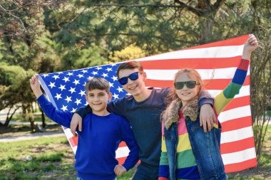 Üç genç çocuk bir arada duruyor ve Amerikan bayrağını geride tutuyorlar..