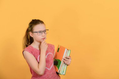 Sarı arka planda gözlüklü, şaşırmış ve düşünceli bir kız elinde kitap ve ders kitapları tutuyor..