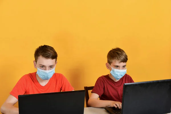 Boys in medical masks are on distance learning and are sitting in front of a laptop monitor, due to the threat of a coronavirus pandemic.