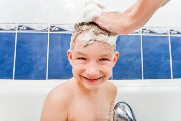 Mom washes the head of a joyful boy with shampoo.
