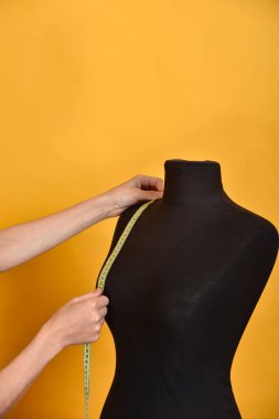 Kadın, turuncu arka planda santimetre olan siyah bir mankeni ölçer..