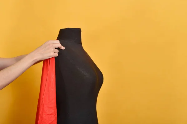 Woman trying on a red big cloth on a black mannequin.