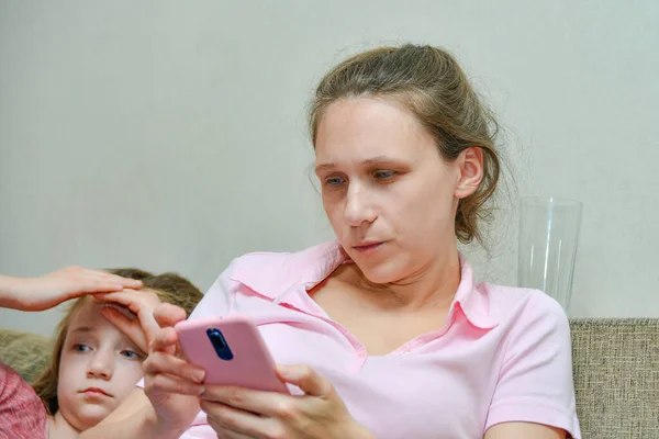 A woman is sitting with a phone on a sofa at home.
