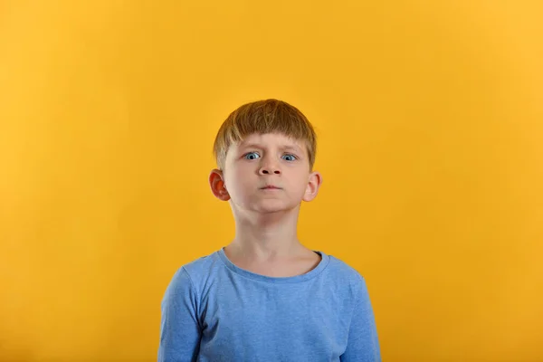 A boy in a blue T-shirt and on an orange background posing.