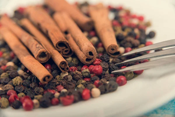 Cinnamon and spices lie on a white plate, a fork lies nearby. Cinnamon and spice grains closeup