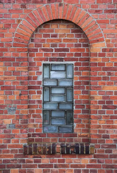 Arco em uma parede feita de tijolos vermelhos com um pequeno elemento de vidro — Fotografia de Stock